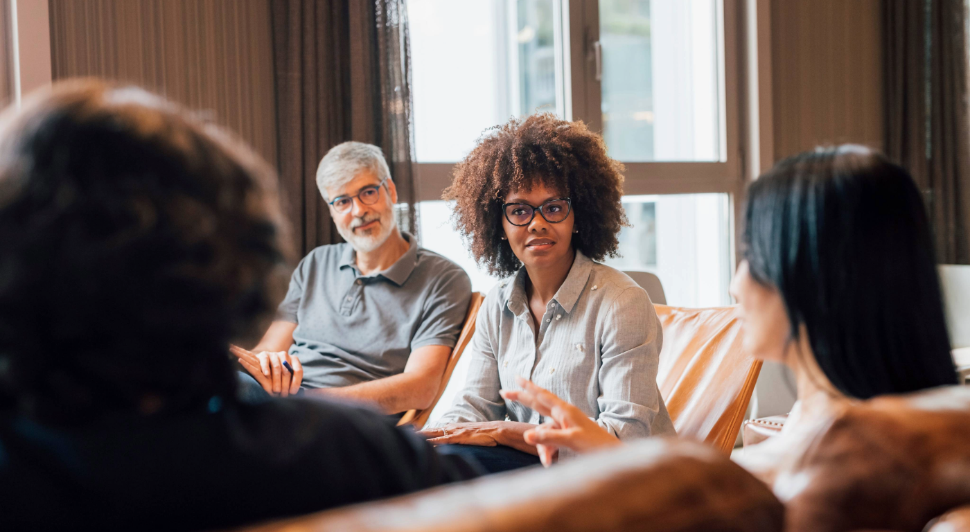 Small group of adults in a meeting, seated in a circle and actively discussing a topic, representing a condo board or community association conversation and decision-making.